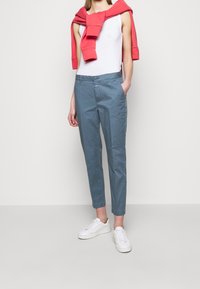 Chinos de algodón azul claro con un corte ajustado, que cuentan con bolsillos laterales y cierre de botón, combinados con zapatillas blancas y un sudadero rojo caído de manera casual.