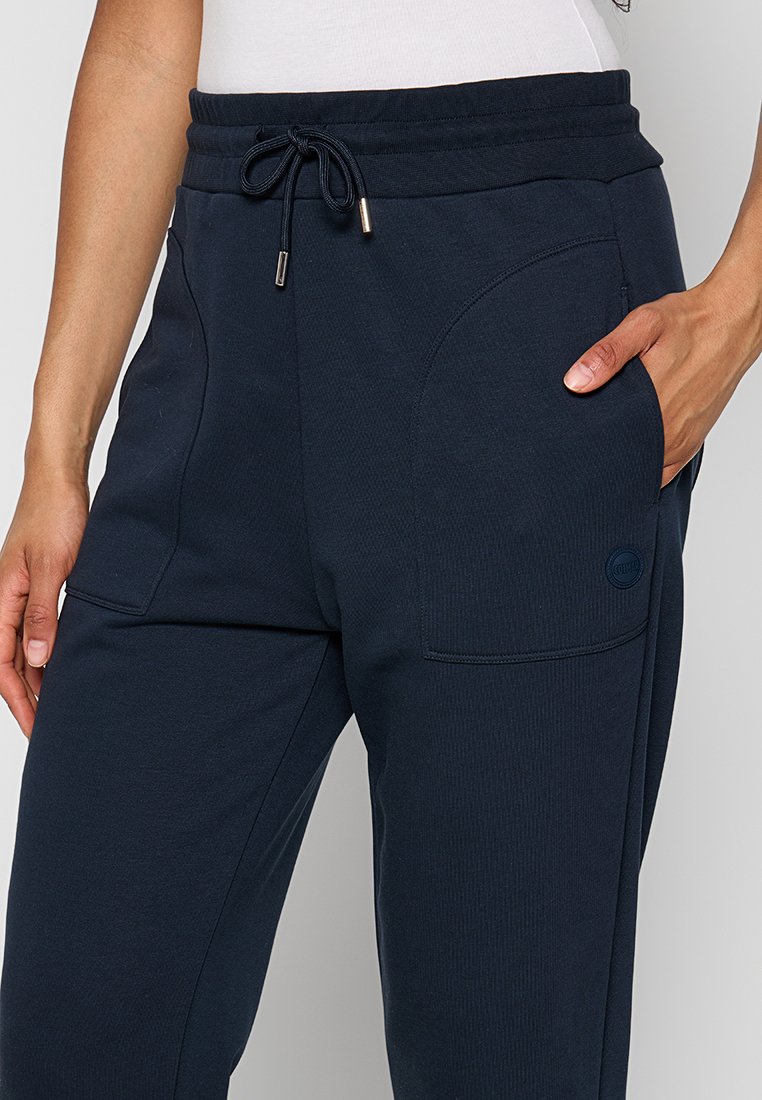 Dunkelblaue Jogginghosen mit gerippter Textur, Kordelzugbund und Seitentaschen. Mit einem dezenten Logo an der Tasche für die Markenkennzeichnung.