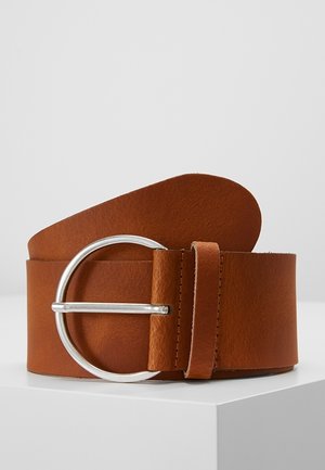 Ceinture en cuir marron avec une boucle ronde argentée, roulée et affichée sur une surface blanche sur un fond gris.