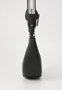 Bolso de cuero negro con forma triangular, superficie texturizada y una correa blanca contrastante que presenta un logo negro y detalles de acento.