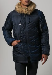 Navy blue padded jacket with a fur-trimmed hood, double-breasted buttons, and zippered pocket, showcasing a glossy, textured finish.