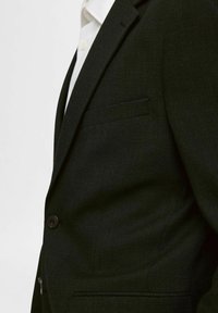 Czarna marynarka o dopasowanym kroju, wykonana z teksturowanej tkaniny, z pojedynczym zapięciem na guzik i kieszenią na piersi. Posiada klapy o wyciętym kształcie.