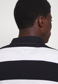 Polo shirt à rayures noires et blanches, avec un col côtelé et un détail de couture triangulaire à l'arrière, en tissu texturé.