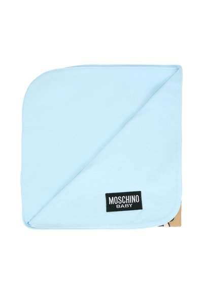 Jasnoniebieski bawełniany kocyk dla niemowląt z diagonalnie złożonym rogiem, zdobiony czarną metką z białym napisem "MOSCHINO BABY". Miękka faktura.