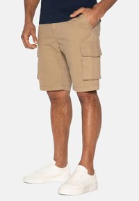 Shorts cargo beiges avec plusieurs poches, une coupe décontractée et des détails cousus. Associés à des baskets blanches pour un contraste.