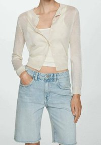 Světle béžový, průhledný cardigan s kulatým výstřihem a zapínáním na knoflíky, ve spojení s vysokými modrými džíny s roztrhaným lemem.