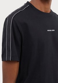 T-shirt en coton noir à manches courtes. Arbore le logo "MICHAEL KORS" en blanc sur la poitrine et un branding texturé le long de la couture de l'épaule.