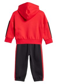 Czerwony sweatshirt z kapturem i czarnymi paskami akcentującymi, w połączeniu z czarnymi dresami z czerwonymi bocznymi paskami. Wykonany z miękkiego, teksturowanego materiału.