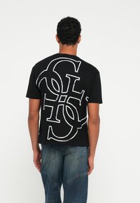 Czarny t-shirt z bawełny z dużym białym napisem graficznym z tyłu. Krótkie rękawy, luźny krój i okrągły dekolt.