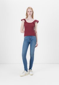 Maroon smocked tank top with ruffled straps paired with blue skinny jeans and white sneakers. Simple, fitted design with a textured finish.