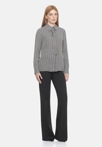 Blusa a maniche lunghe con motivo bianco e nero, dotata di colletto, abbinata a pantaloni neri a gamba larga, su uno sfondo neutro.