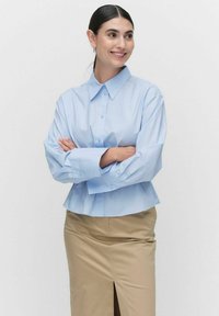 Jasnoniebieska, długosleeve koszula z guzikami, o spiczastym kołnierzu, luźnym kroju i mankietami, połączona z beżową spódnicą z przednim rozcięciem.