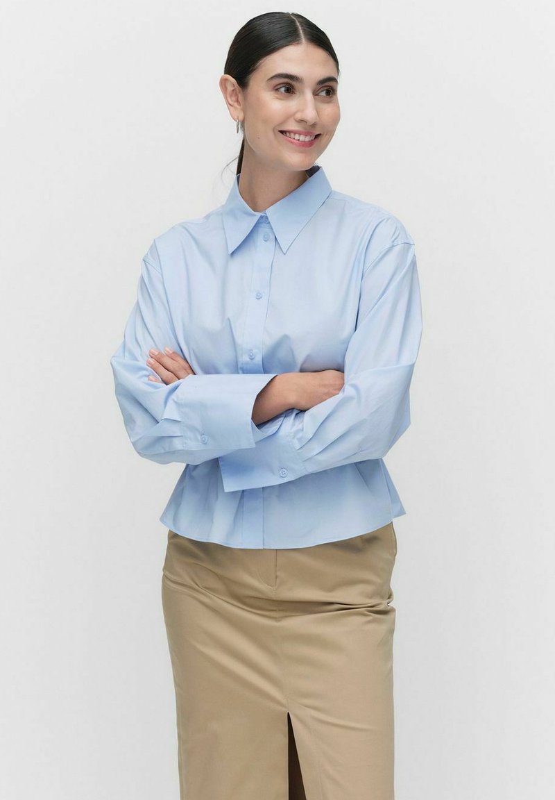 Jasnoniebieska, długosleeve koszula z guzikami, o spiczastym kołnierzu, luźnym kroju i mankietami, połączona z beżową spódnicą z przednim rozcięciem.