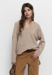 Beige, over-sized sweater med V-udskæring, ribbede manchetter og blød tekstur, sammen med lysebrune bukser med sidelommer.