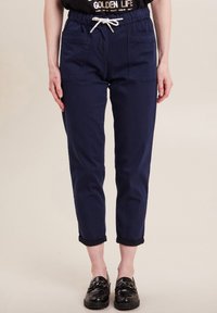 Marineblauwe joggerbroeken met een elastische tailleband en witte trekkoord. Beschikt over twee frontzakken en opgerolde manchetten. Gladde katoenen stof.