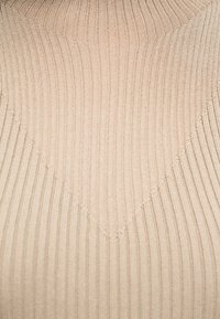 Tissu beige en maille côtelée formant un motif en chevrons avec des lignes verticales et diagonales.