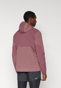 Αδιάβροχο μπουφάν σε διαβάθμιση ροζ και μωβ, με κουκούλα, ρυθμιζόμενο τελείωμα και πλαϊνές τσέπες για λειτουργικότητα.