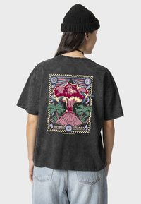 Camiseta de algodón gris con un corte relajado, que presenta un gráfico colorido de un volcán en erupción y palmeras en la parte posterior.