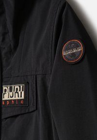 Giacca nera con tessuto strutturato. Presenta una patch con il logo "Napapijri" e dettagli arancioni. Include una tasca laterale e cuciture in evidenza.