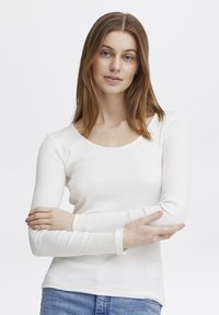 Hvit langermet topp med ribbestruktur, rund hals og tettsittende ermer; sammen med lyseblå denimjeans.