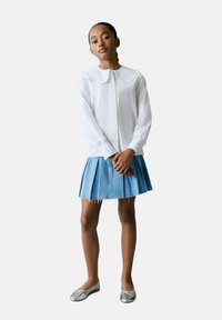 Cămașă albă cu guler mare, asociată cu o fustă din denim plisată și balerini gri. Material neted cu un design curat.