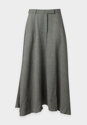 Vrouw staand, draagt een witte lange-mouwen blouse en een grijze, hoog getailleerde, enkellange rok met zwarte platte schoenen.