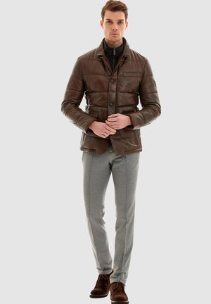 Brown leather puffer jacket with a collared neckline, front buttons, and chest pocket. Paired with light gray trousers and brown shoes.