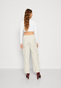 Hvit langermet crop-top kombinert med beige cargo-bukser med sidelommer; modell iført burgunder høye hæler, med langt bølgete hår synlig.