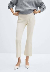 Vaqueros acampanados beige de denim, con una cintura alta y dobladillos deshilachados, combinados con un suéter de punto gris y tacones blancos de punta. 