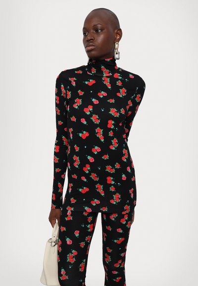 Haut noir à manches longues avec un col montant, orné d'un motif floral rouge et vert, associé à des leggings assortis. Tissu doux et design ajusté.