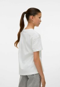 T-shirt en coton blanc avec une coupe décontractée, des manches courtes et un col rond, associé à un pantalon gris clair à coupe ample.