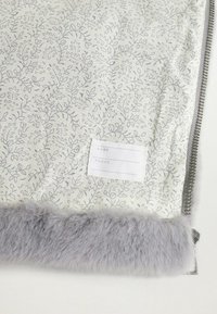 Materiał w kwiatowy wzór w jasnym kremie z szarymi akcentami, z miękkim szarym futrzanym wykończeniem oraz białą metką na dane osobowe i telefon.