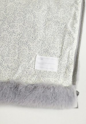 Blomsterpræget stof i lys creme med grå accenter, udstyret med en blød grå pelskant og et hvidt mærke til navn og telefonoplysninger.
