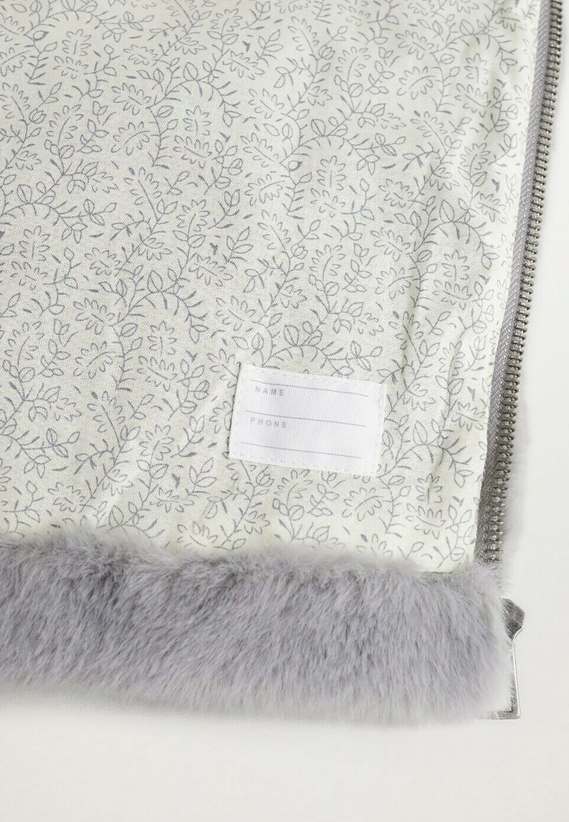 Materiał w kwiatowy wzór w jasnym kremie z szarymi akcentami, z miękkim szarym futrzanym wykończeniem oraz białą metką na dane osobowe i telefon.
