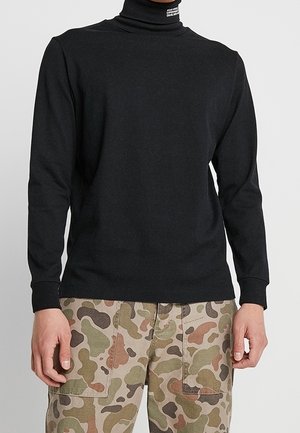 Maglione nero a maniche lunghe con collo alto realizzato in un tessuto liscio e stretch; design aderente con polsini rinforzati, indossato con pantaloni cargo a motivo mimetico.