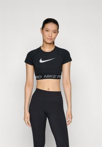 Musthave musträtik, mis on ümmarguse kaelusega ja lühikeste varrukatega, millel on valge Nike logo ning must vöö, millel on valgete tähtedega "PRO", koos mustade retuusidega.