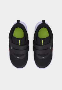 Ζευγάρι μαύρα αθλητικά παπούτσια με πράσινες εσωτερικές σόλες, λευκές εξωτερικές σόλες, λουράκια με βέλκρο και μικρά λευκά λογότυπα Nike στα δάχτυλα και στα κορδόνια.