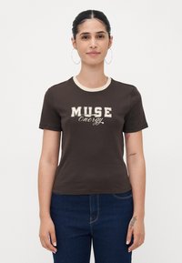 Rudas medvilninis marškinėliai su smėlio spalvos apykakle, puikuojantis užrašu "MUSE Energy" kremine ir rudąja rašysena. Trumpomis rankovėmis ir prilipusio kirpimo.