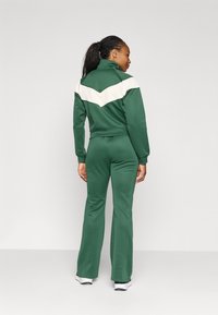 Tuta verde realizzato in tessuto liscio con colletto alto e un motivo a zigzag crema contrastante sulla schiena. Design aderente con pantaloni svasati.