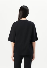 T-shirt en coton noir avec une coupe décontractée, des manches courtes et un col rond. Texture lisse, sans motifs ni éléments métalliques visibles. Design simple.