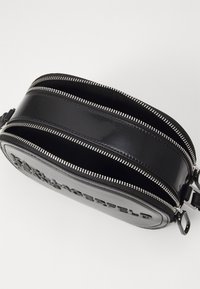 Borsa in pelle verniciata nera con doppie tasche con zip, dotata di accessori in argento e logo in rilievo su un lato, con superficie liscia.