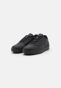 Black athletic shoes made of synthetic leather with a flat sole, round toe, and lace-up design. Features perforated detailing and logo accent.
