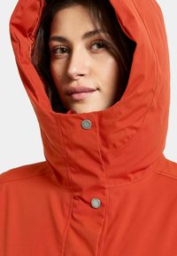 Orange hooded jacket featuring a high collar, snaps, and smooth fabric texture, designed for warmth and protection against the elements.