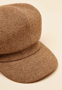 Pruun herringbone-mustriga nokamüts tekstuurse kangaga, millel on lame kroon ja lai, kergelt kaarduv ääreosa.