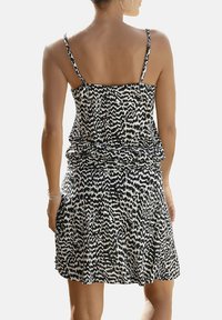 Svartvit mönstrad klänning med tunna axelband och avslappnad passform, med en rynkad midja och utsvängd kjol. Slät tygstruktur.