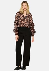 Blusa con stampa leopardata, maniche a palloncino, scollo a V e tessuto trasparente, abbinata a pantaloni neri a vita alta e scarpe nere.