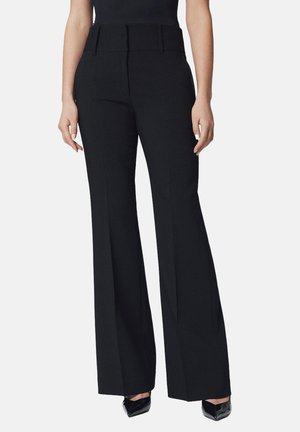Czarne spodnie o szerokich nogawkach i wysokim stanie, z płaskimi kieszeniami z przodu i gładką strukturą, zestawione z czarnymi szpilkami.