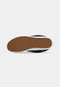 Svart skatesko med en teksturert gummisåle som har et bikake-mønster, hvit mellomsåle og slank profildesign.