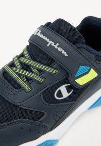Scarpe da ginnastica blu scuro realizzate in rete e materiale sintetico, con lacci verde neon, un logo bianco e una suola contrastante con dettagli.