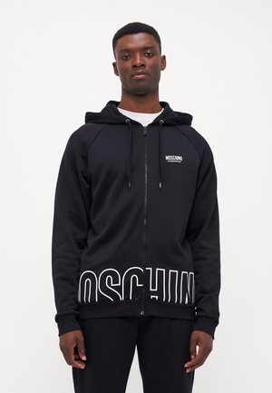 Sweat à capuche noir zippé avec le logo blanc "MOSCHINO" en bas et sur la poitrine, doté d'une capuche à cordon de serrage et de poignets et d'une taille côtelés.